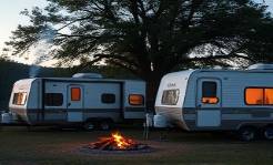 Quaint Connecticut trailers, cozy, stationed at a rural campsite, photorealistic, amidst rolling fields and towering oak trees, highly detailed, smoke from a campfire wafting in the air, 4k resolution, earthy colors, twilight lighting, shot with a 50mm lens.